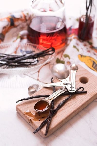 vanilla extract in a measuring spoon with vanilla beans and a bottle of vanilla extract in the background