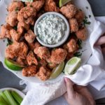 two hands serving a platter of cauliflower wings