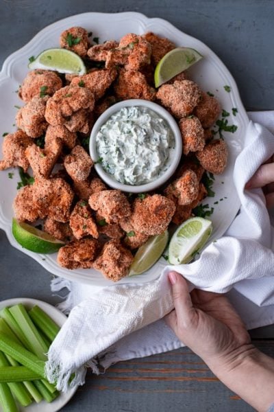 two hands serving a platter of cauliflower wings
