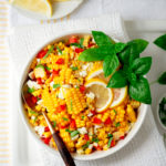 summer corn salad in a bowl with serving spoon and lemon wheels and basil tops for garnish